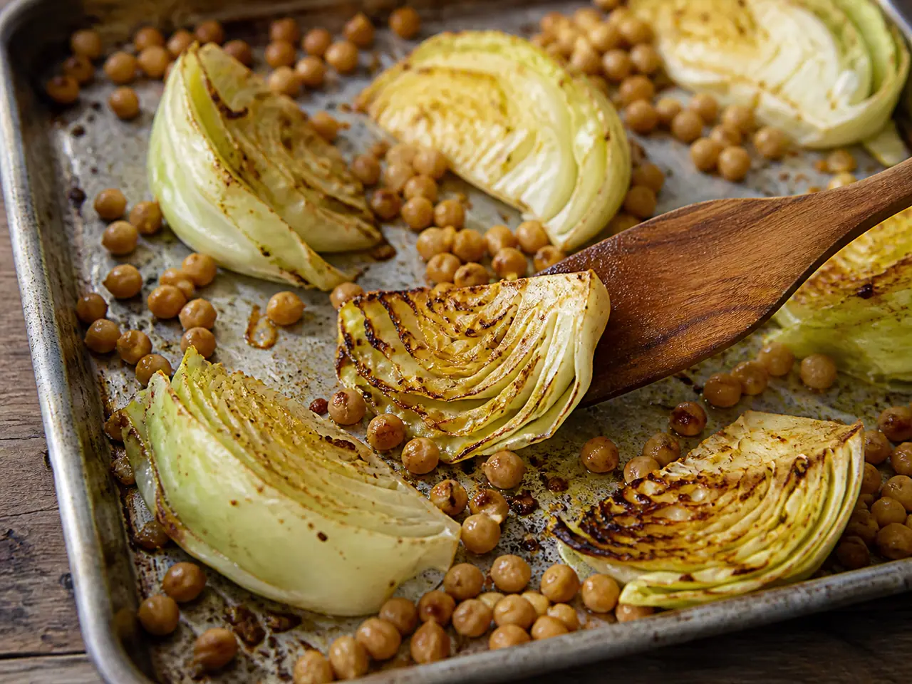 Roasted cabbage wedges and chickpeas being turned on a hot tray