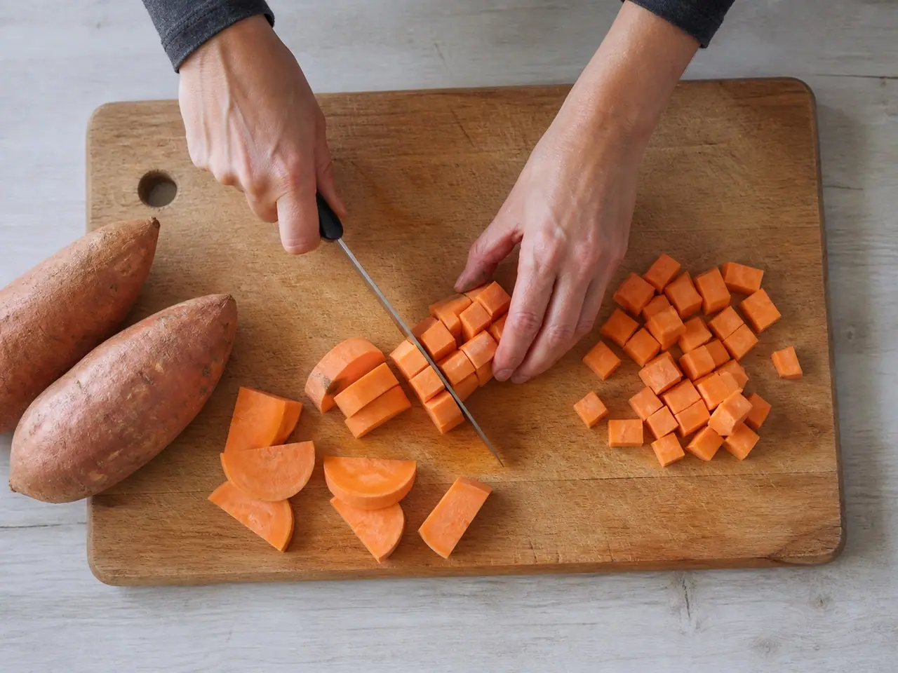 Hands cutting sweet potatoes into thick dinner-size pieces