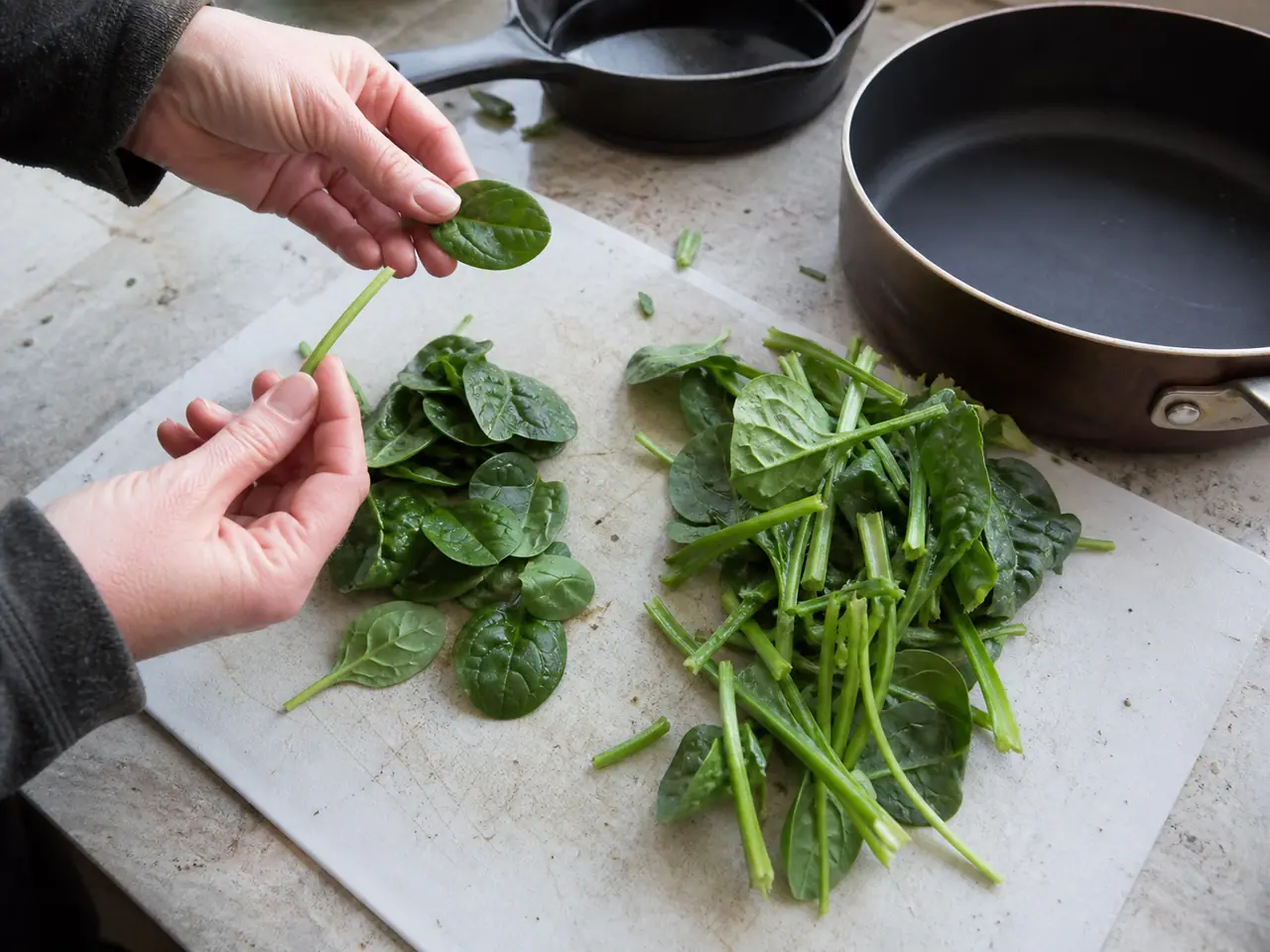Hands comparing baby spinach and mature leaves before cooking