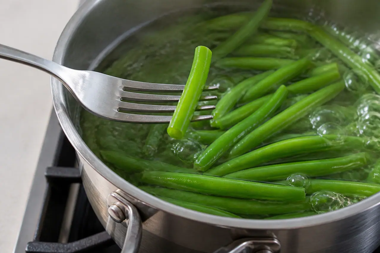 A fork testing green beans at the edge of a saucepan