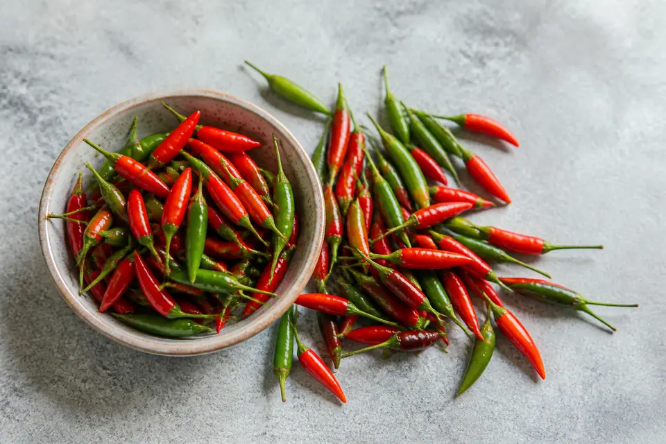 Red and green bird's eye chillies scattered beside a small bowl
