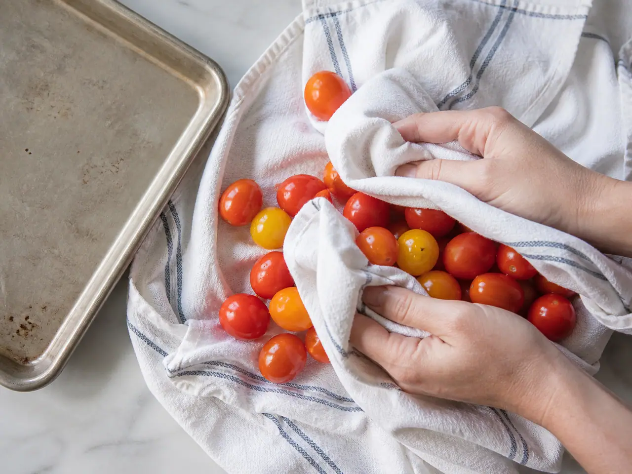 Hands drying washed cherry tomatoes on a clean tea towel