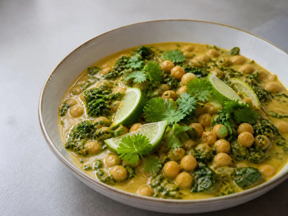 Portion of coconut chickpea curry with fresh greens and lime