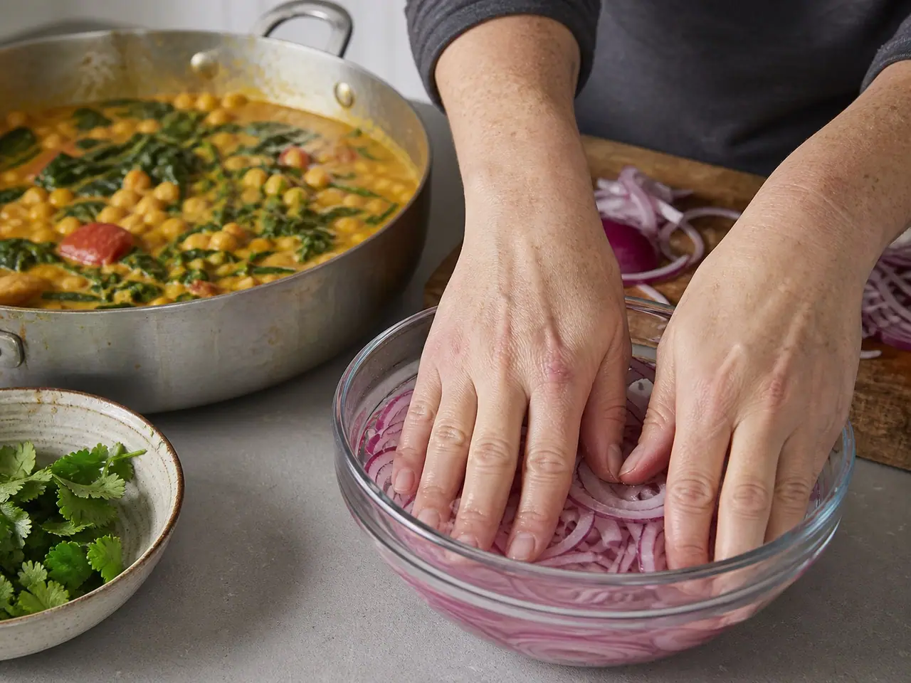 Hands pressing thin red onion slices into quick pickle brine