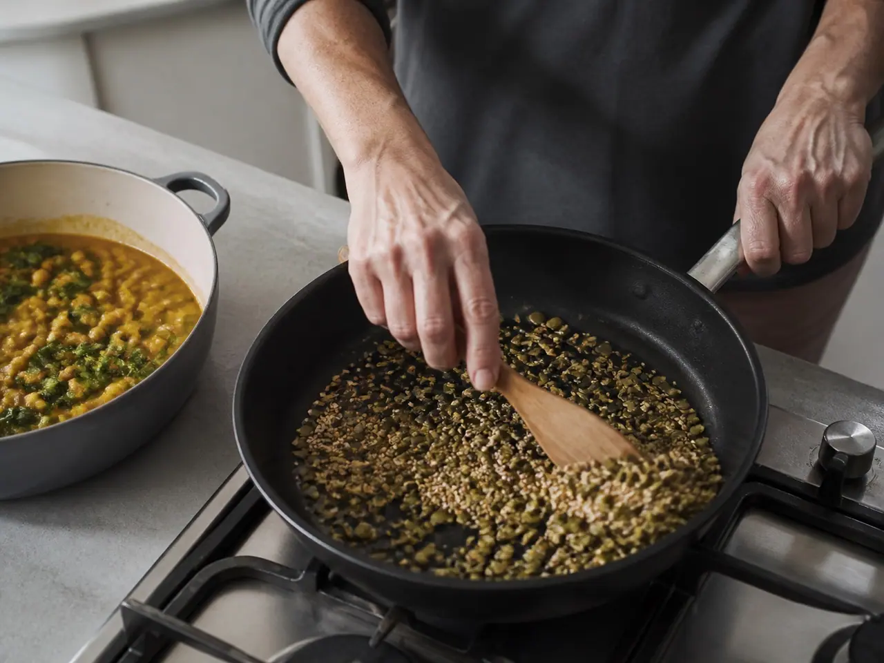 Hands tossing pumpkin and sesame seeds in a dry frying pan