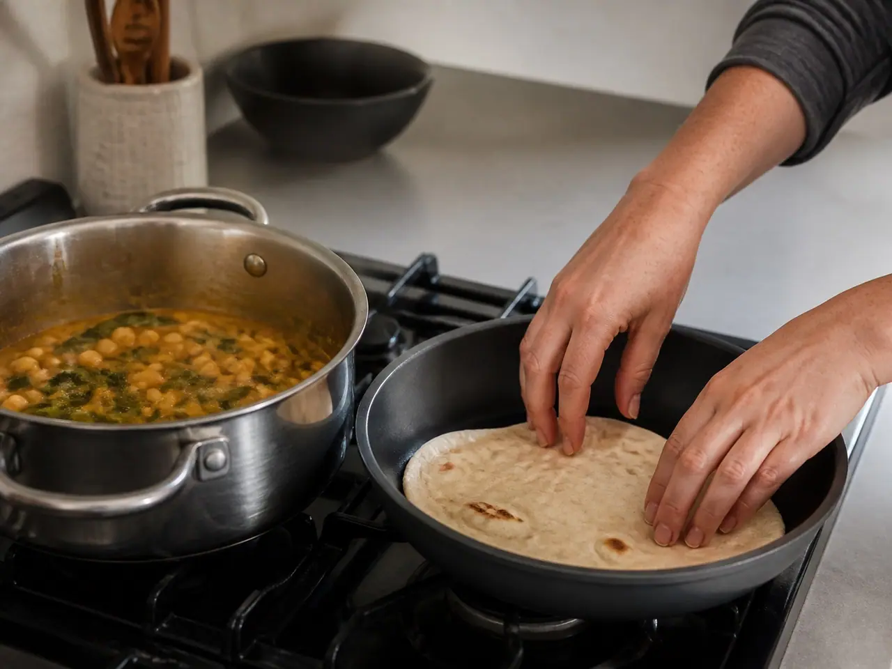 Hands warming flatbread in a dry pan beside simmering chickpea curry