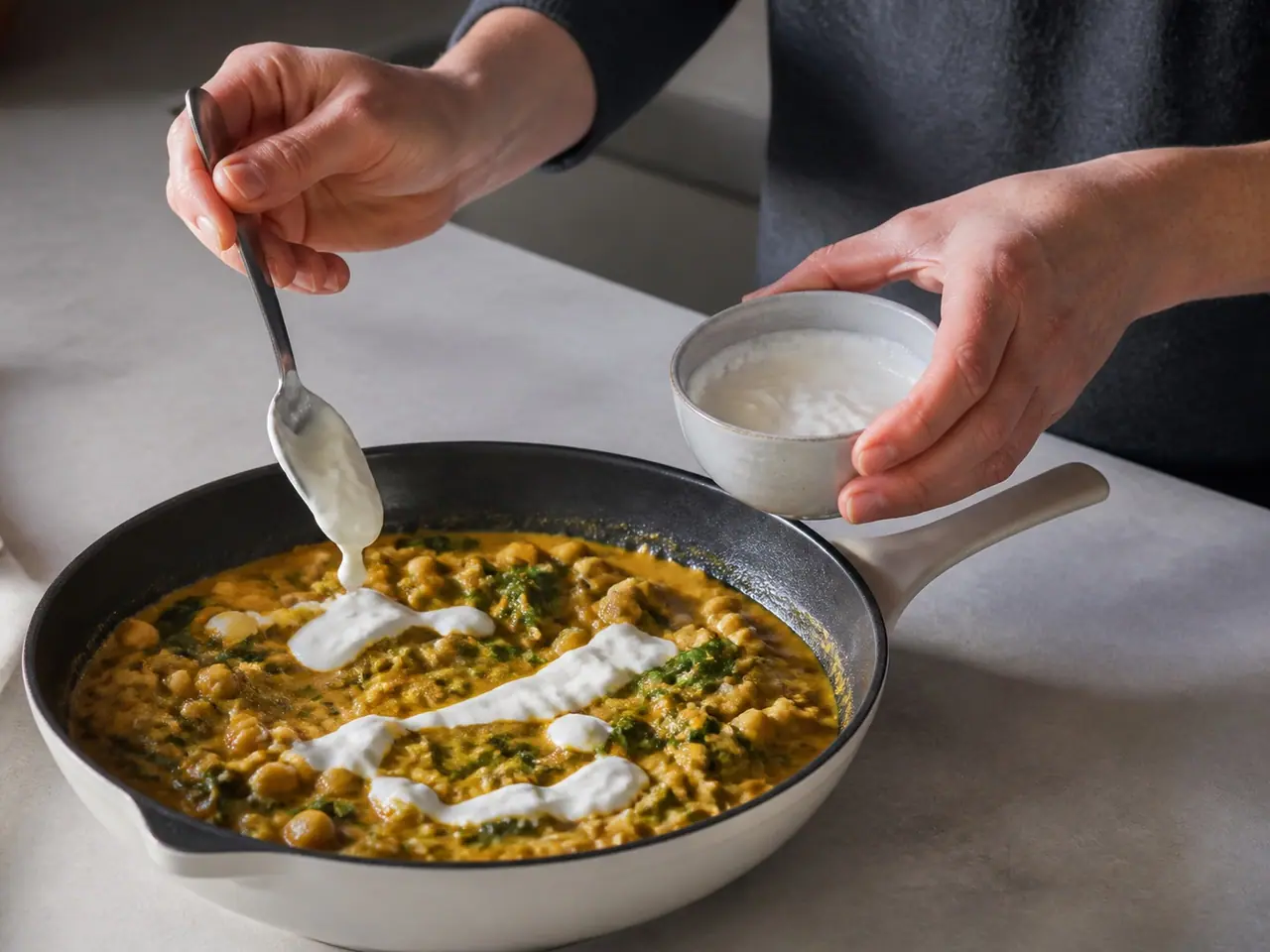 Hands spooning lemon yogurt beside a simmering coconut chickpea curry