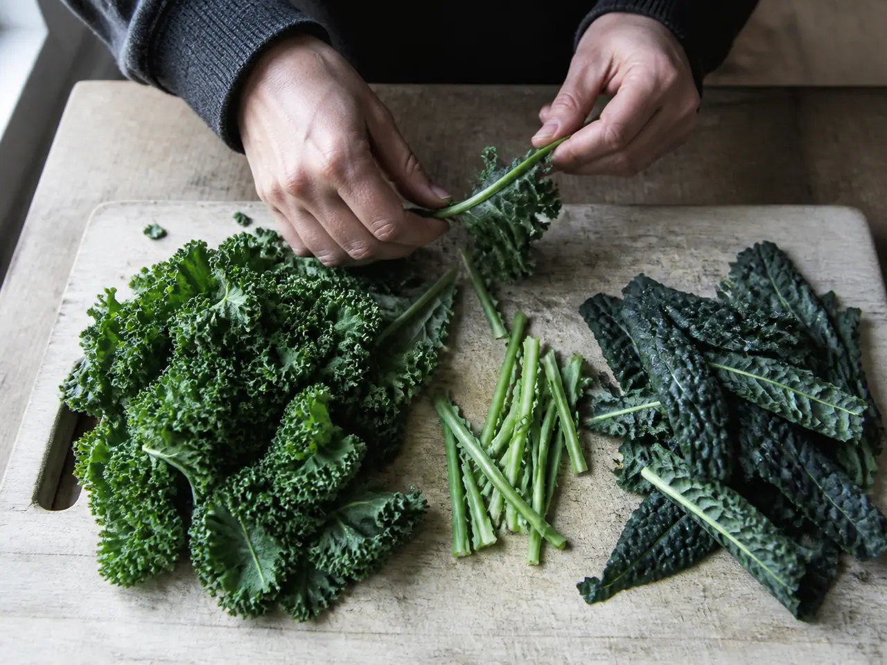 Hands stripping curly kale and cavolo nero from their stems