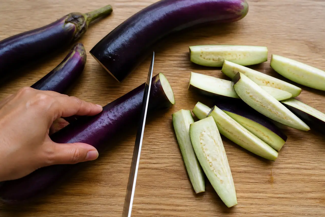 Hands cutting globe and long aubergines into roasting wedges