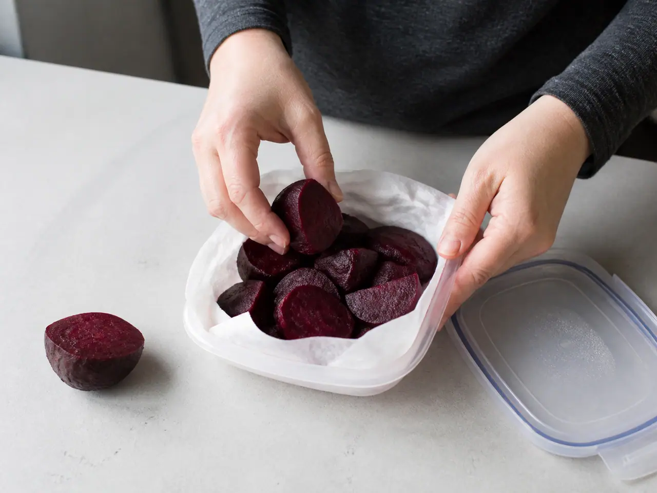 Hands peeling and packing cooked beetroot into a covered container