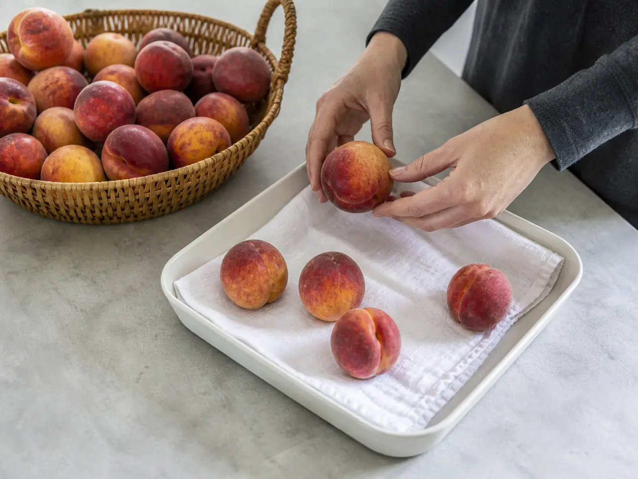 Hands lifting ripe peaches by the shoulder into a shallow container