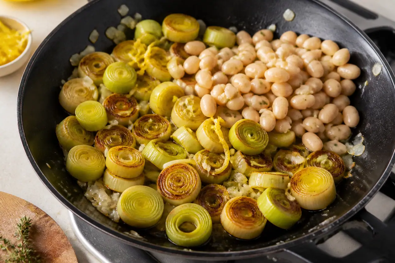 Leek rounds browning in a skillet beside white beans and lemon