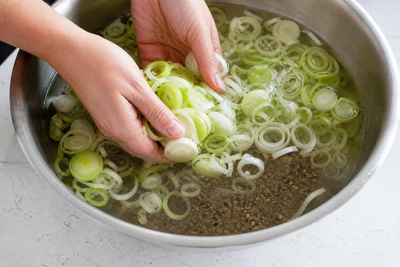 Sliced leeks rinsing in water beside an onion and a skillet