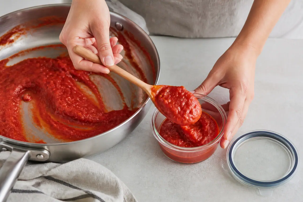 Hands spooning leftover tomato sauce into a container