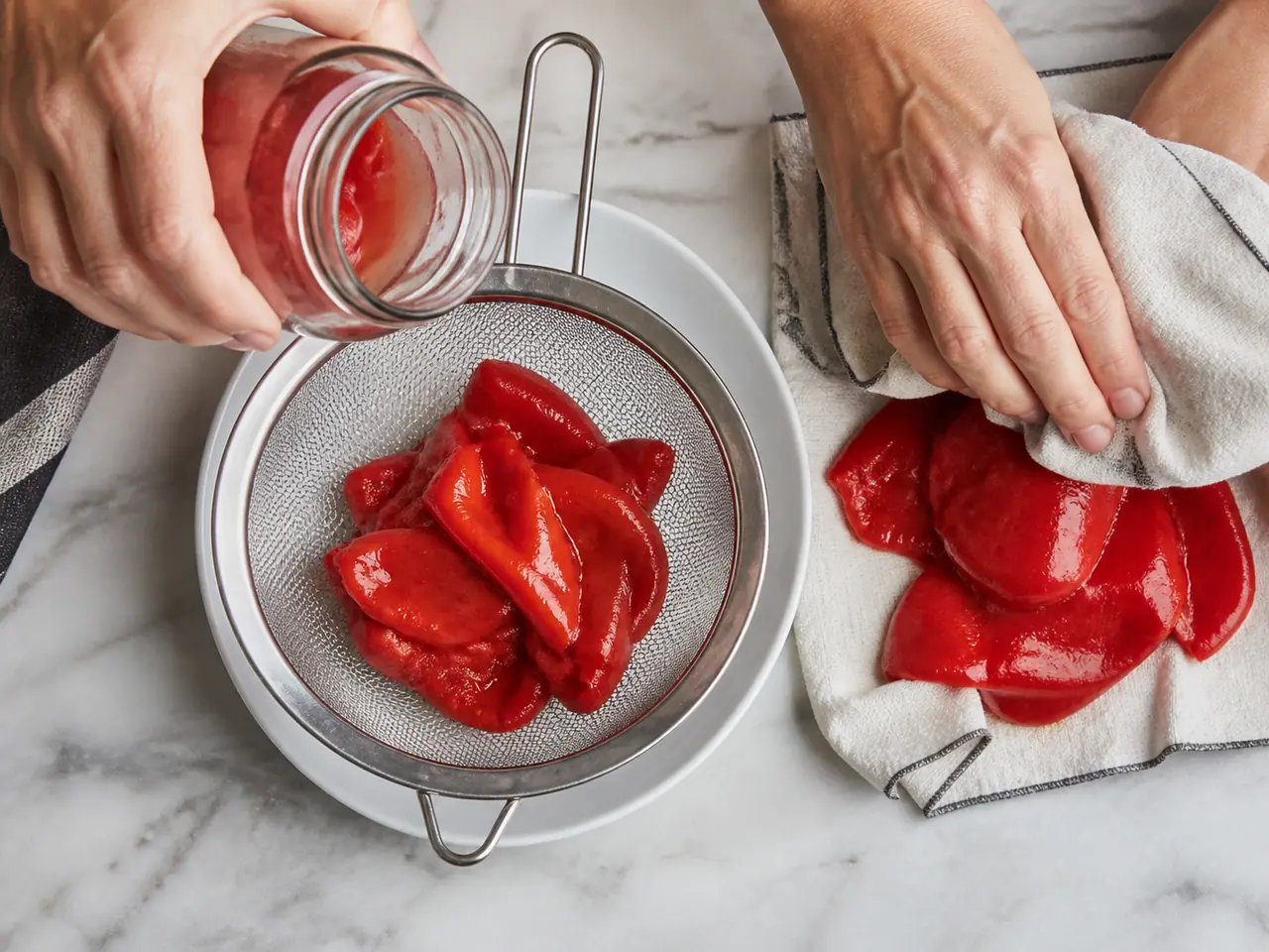 Hands draining jarred piquillo peppers in a fine sieve
