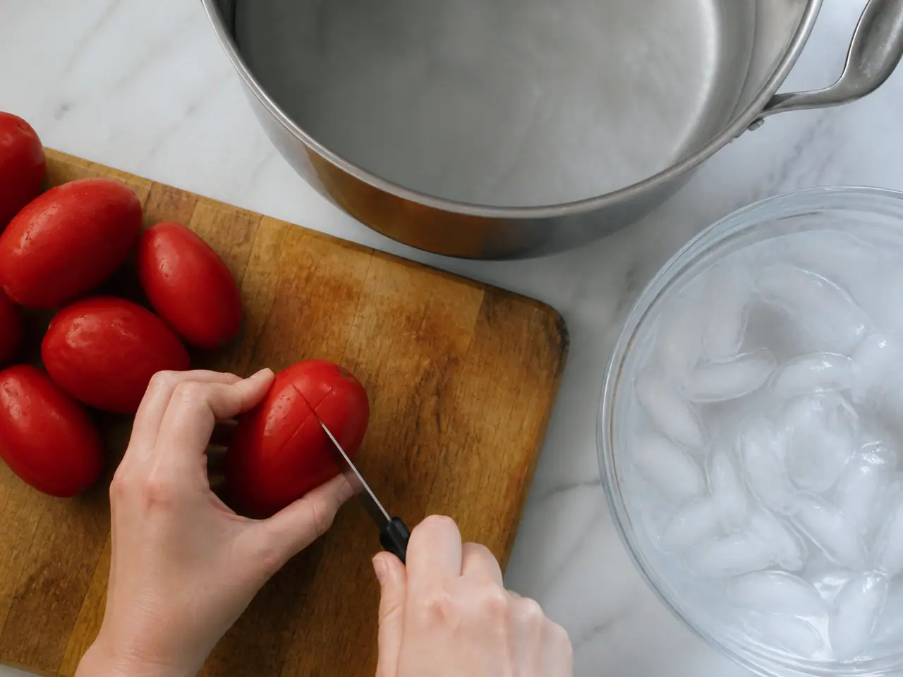 Hands scoring plum tomato skins before blanching in hot water