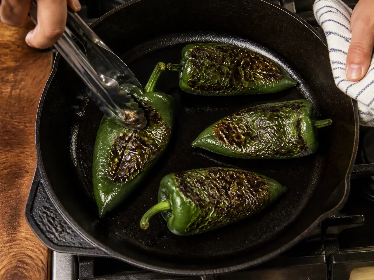 Hands charring poblano peppers in a dry cast iron skillet