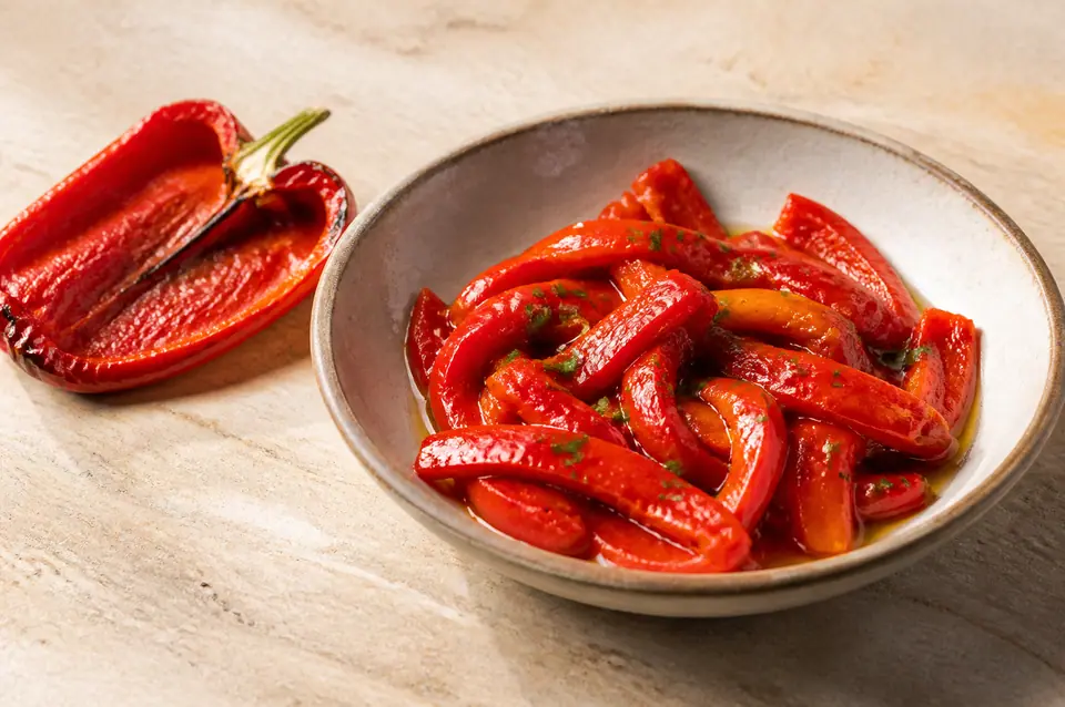 Glossy roasted red pepper strips with parsley in a shallow dish