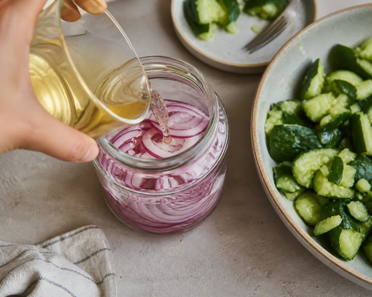 Hands preparing quick pickled red onions smashed cucumber and peanut salad during the start the pickles step