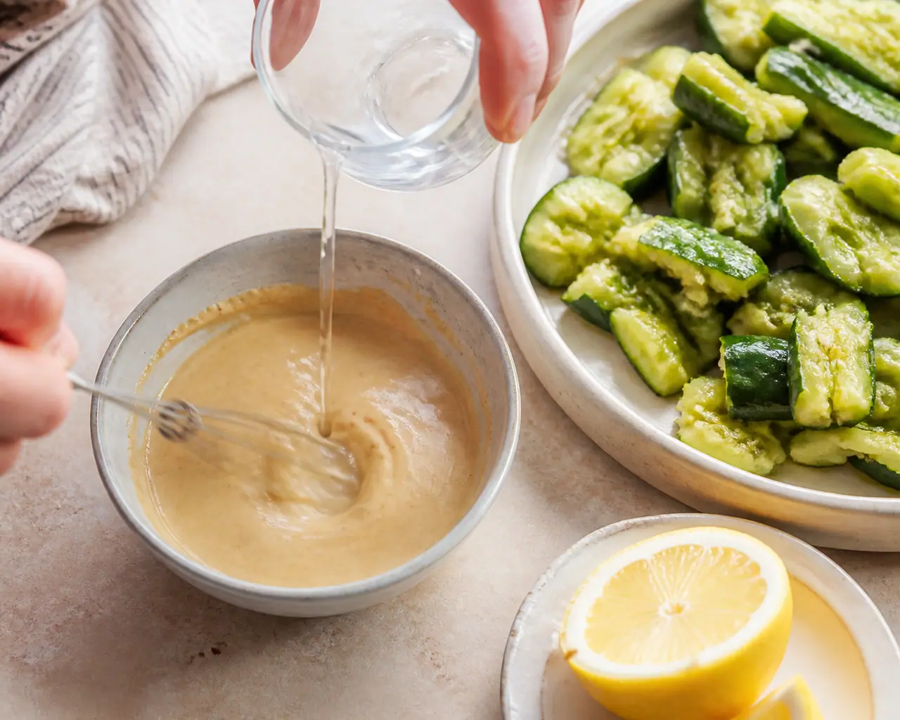 Hands preparing lemon tahini dressing smashed cucumber and peanut salad during the loosen the tahini step