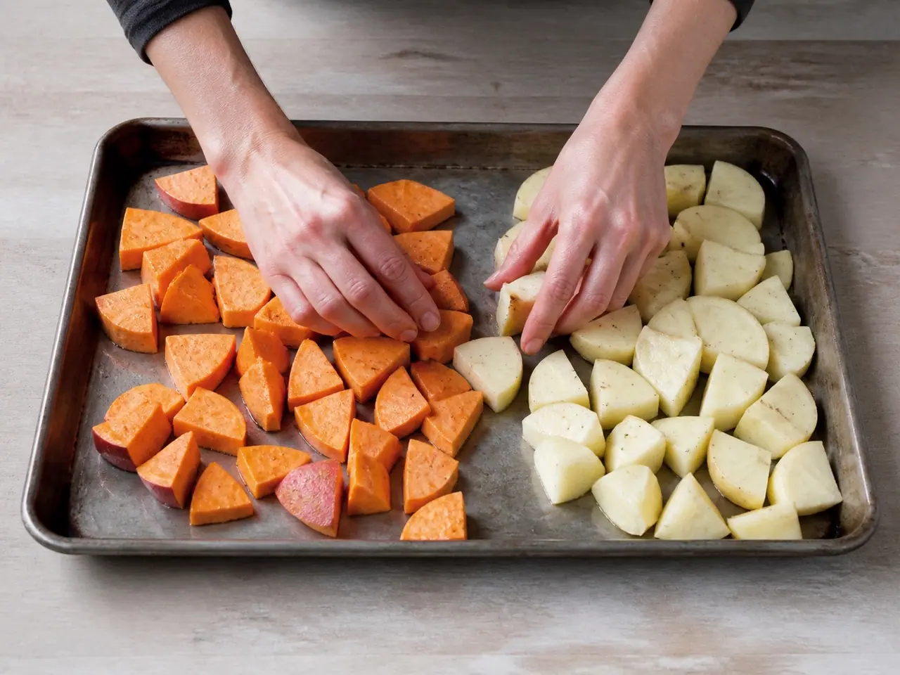 Hands arranging sweet and white potato pieces on a hot tray