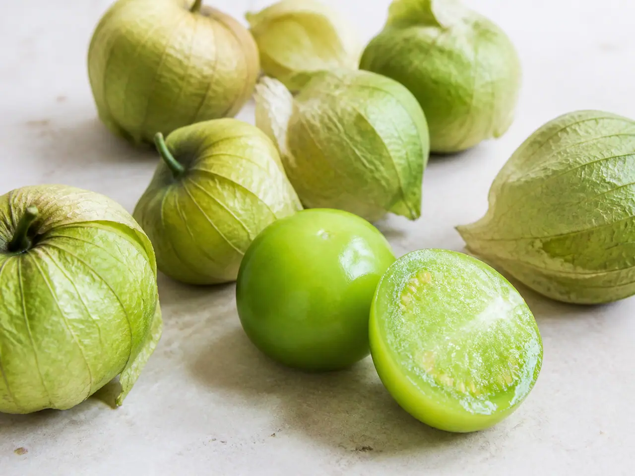 Fresh tomatillos in husks beside peeled green fruit
