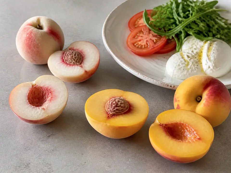 White and yellow peaches cut open beside a summer plate