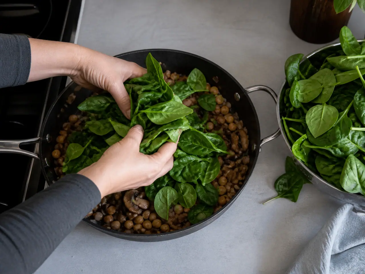 Hands folding fresh spinach into a wide skillet