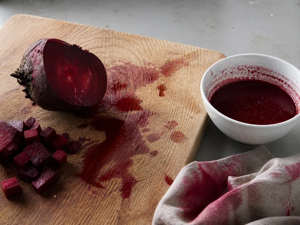 Deep red beetroot juice staining a board beside cooked beetroot