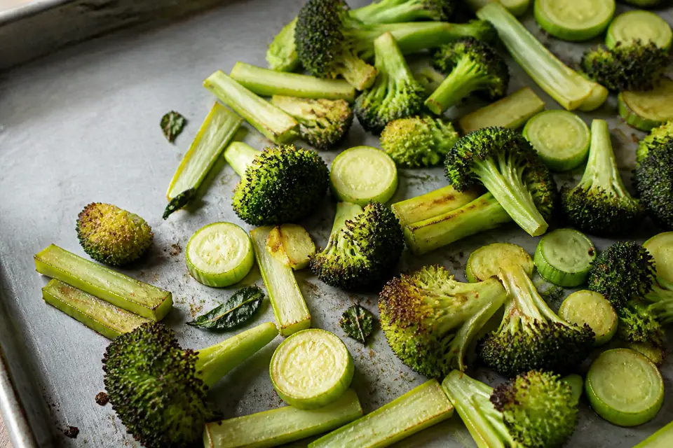 Roasted broccoli florets and sliced stems on a dark baking tray