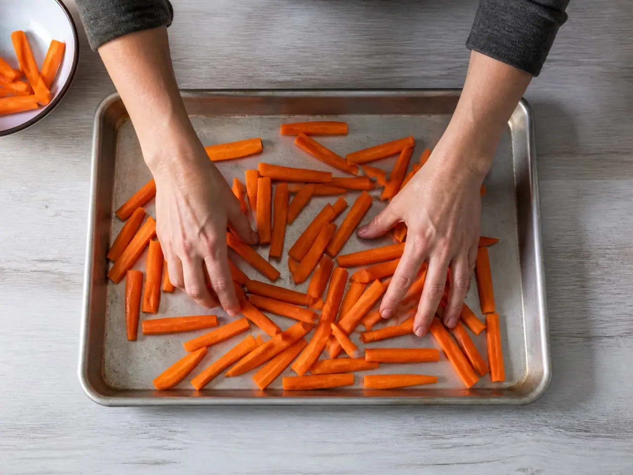 Hands spreading carrot batons across a baking tray