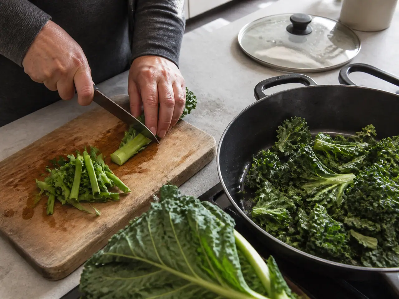Hands slicing kale ribs before adding the leaves to a pan
