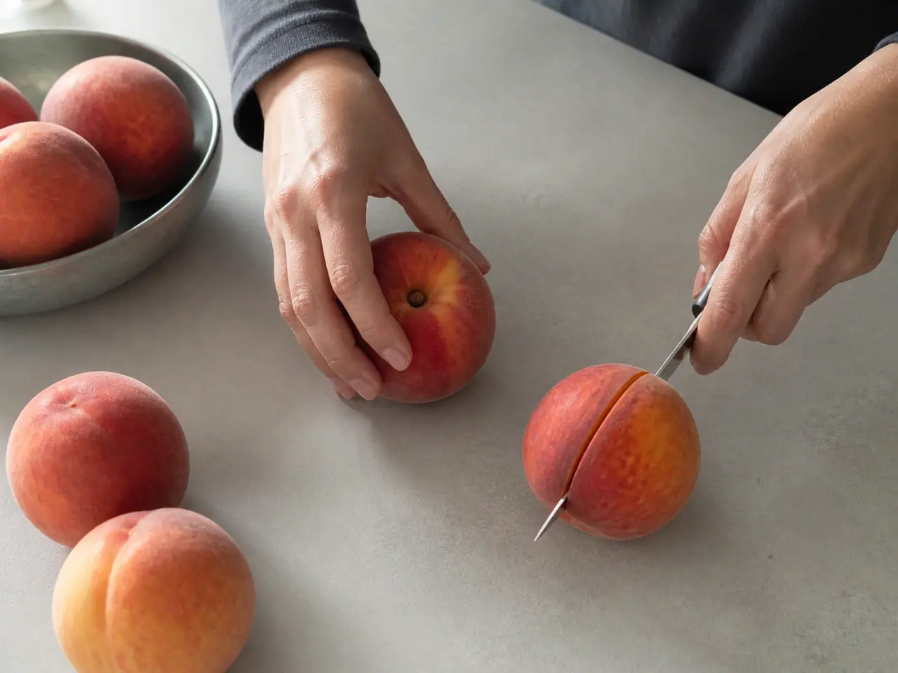 Hands testing peach firmness near the stem before slicing