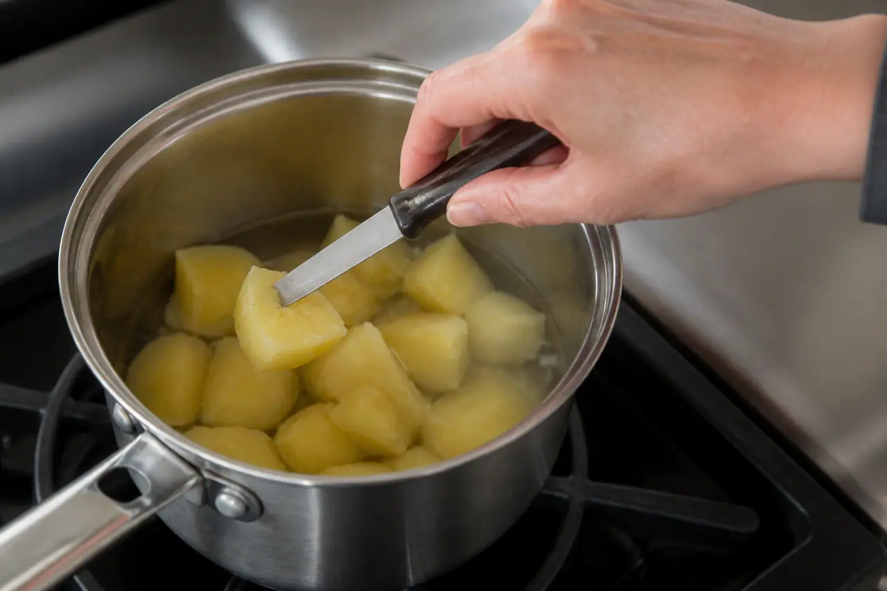 Hand testing the centre of the largest potato piece with a small knife